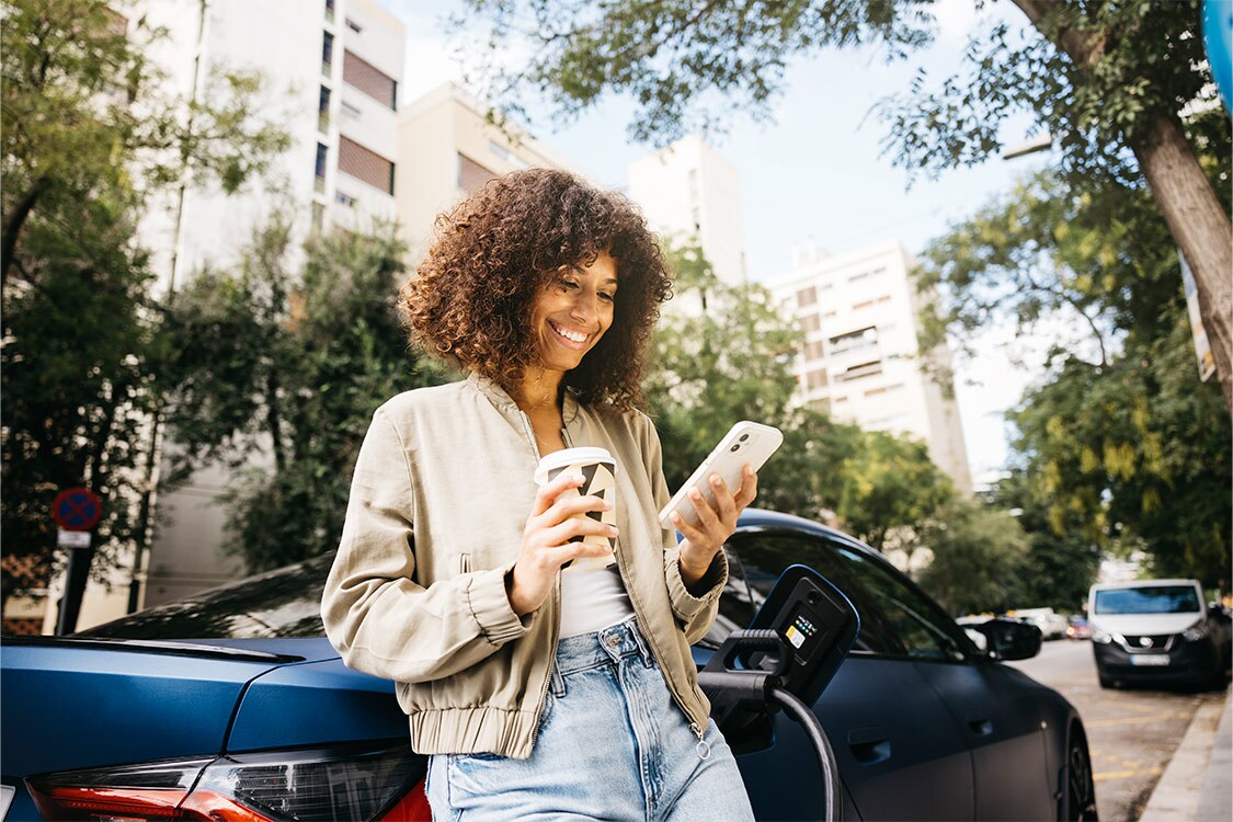 Woman smiling while charging an electric car in a sustainable city.