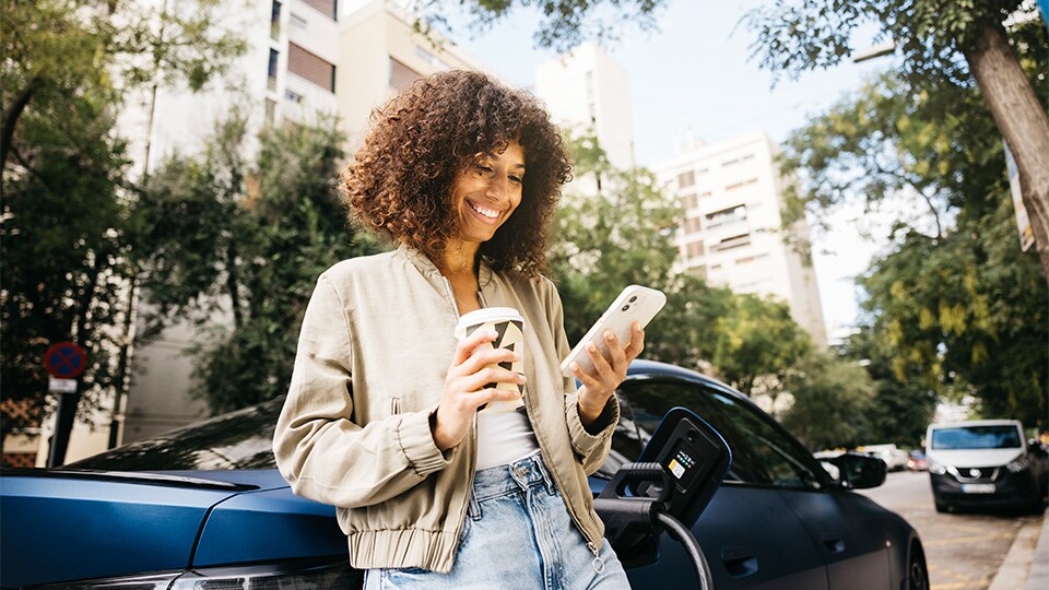 Mulher a sorrir enquanto carrega um carro elétrico numa cidade sustentável.